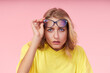 Portrait of young excited woman in glasses, yellow casual t-shirt on pink background. Surprised and incredulous looks wide open mouth and eyes