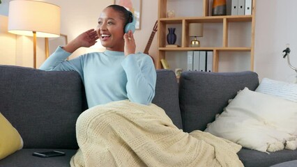 Wall Mural - Comfortable, fun and relaxing young woman using her phone and headphones to listen to music at home. Female resting on a couch scrolling an app in her house. Lady sitting on a sofa enjoying tunes