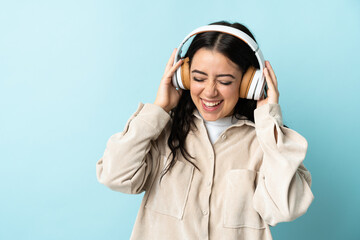 Wall Mural - Young caucasian woman isolated on blue background listening music