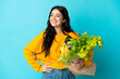 © luismolinero - Young woman holding a grocery shopping bag isolated on blue background posing with arms at hip and smiling