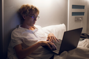 Young man lies in bed open laptop night watching internet movies