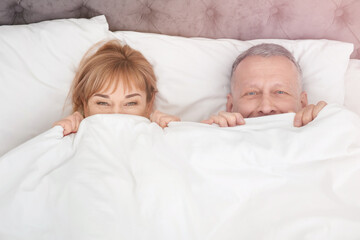 Poster - Mature couple hiding together under blanket in bed at home