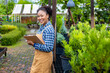 African American gardener holding clipboard while working in her conifer tree nursery garden center for evergreen and bonsai artist supply concept
