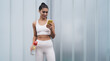© BullRun - Portrait of young smiling female in wireless earphones standing with mobile phone device on copy space background. Attractive brunette woman with fit figure controls physical activity using mobile app