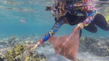 Woman in diving equipment swims and collects plastic debris underwater on the bottom of coral reef. Snorkeler cleaning Ocean from plastic pollution. Plastic pollution of the Ocean. Red sea, Egypt