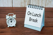 On lunch break text on white table calendar with alarm clock pointing at 12pm. Office and business concept