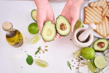 Wall Mural - Making avocado toast - Woman hold fresh ripe halved avocado