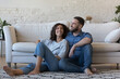 © fizkes - Happy dreamy married couple enjoying comfort, leisure at home, relaxing together on heating carpeted floor. Husband and wife enjoying hugging, talking, laughing, discussing new comfortable apartment