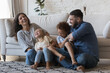 Happy parents cuddling, tickling little children on floor, laughing, having fun, enjoying family activity, leisure. Cheerful excited mom and dad playing with giggling son and daughter kids at home
