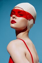A Self-confident Stylish Young Woman In A White Swimming Cap And Red Glasses Looks At The Camera Arrogantly. Headshot In The Studio