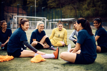 Wall Mural - Team of happy female soccer players and their coach relaxing on grass after sports training.