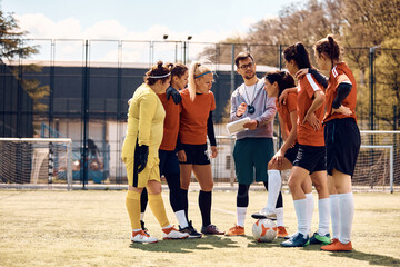 Wall Mural - Soccer coach planning game strategy with female team on playing field.