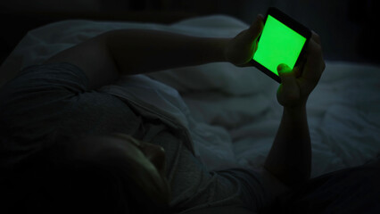 Man uses phone while lying in bed. Concept. Young man lying in bed uses smartphone with green screen. Dependence on smartphones and social networks