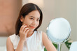 © pixindy - Closeup portrait of smiling young beautiful asian woman looking at mirror touching her skin enjoying treatment for dry skin.