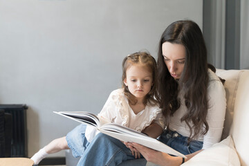 Mom and daughter are reading a book on the sofa. Study and activities with children at home, mental development, free time with children