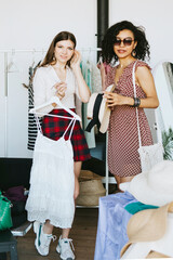 two young woman female caucasian and african students at swap party try on clothes, bags, shoes and accessories, change clothes with each other, second hand for things, zero waste life, eco-friendly