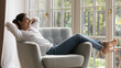© fizkes - Joyful carefree beautiful Indian woman relaxing in comfortable armchair with at big terrace window, feeling lazy, happy, taking deep breath, enjoying leisure, comfort at home. Banner shot