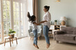 © fizkes - Excited Indian kid and happy mom holding hands, jumping to music on floor. Cheerful mother teaching kid to dance music in living room, smiling, laughing, having fun. Family activity concept