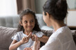 © fizkes - Happy cute Indian kid girl talking to mother, using hands, fingers, speaking sign languages, sitting on sofa at home. Female teacher, therapist teaching child with deafness to communicate