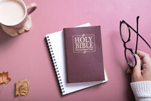 Holy Bible And Female Hand In Sweater With Glasses And A Cup Of Coffee Top View. Holy Bible Study Online Concept