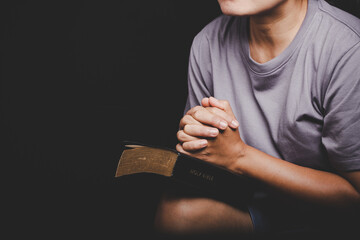 Wall Mural - Close up of christian woman hand on holy bible are pray and worship for thank god in church with black background, concept for faith, spirituality and religion