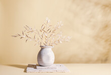 Still Life With White Dried Branches With Leaves In Light Ceramic Vase On Stone Blocks On Pastel Background With Shadows. Home Decoration With Dried Flowers.