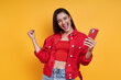 Excited young woman holding smart phone and gesturing while standing against yellow background