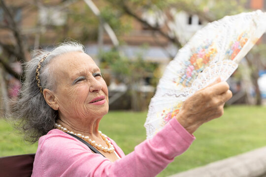 old woman with gray hair using hand fan global heat wave. elderly people suffering from high tempera