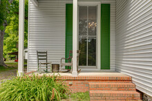 Historic Country Home In Virginia With Covered Porch Rocking Chairs Sunny Day Antique Chairs Brick White Siding With Green Shutters Floor To Ceiling Window