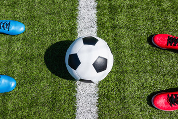 Soccer football background. Soccer ball and two pair of football sports shoes on artificial turf soccer field with shadow from football goal net on sunny day outdoors. Top view