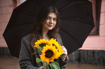 Wall Mural - A young woman with a bouquet of sunflowers under an umbrella in rainy weather.