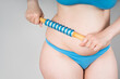Woman with anti-cellulite roller massager on gray background