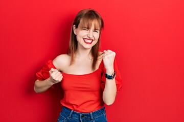 Poster - Redhead young woman wearing casual red t shirt celebrating surprised and amazed for success with arms raised and eyes closed. winner concept.