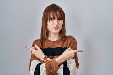 Wall Mural - Young beautiful woman wearing striped sweater over isolated background pointing to both sides with fingers, different direction disagree