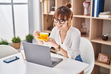 Poster - Young woman using laptop and drinking coffee at home