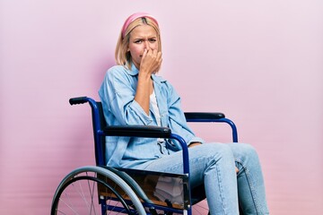 Wall Mural - Beautiful blonde woman sitting on wheelchair smelling something stinky and disgusting, intolerable smell, holding breath with fingers on nose. bad smell