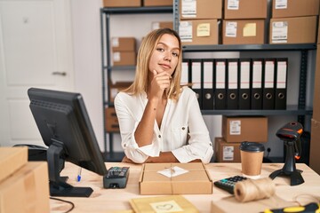 Canvas Print - Young blonde woman working at small business ecommerce looking confident at the camera smiling with crossed arms and hand raised on chin. thinking positive.