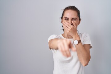 Sticker - Beautiful brunette woman standing over isolated background laughing at you, pointing finger to the camera with hand over mouth, shame expression