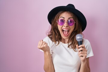 Sticker - Beautiful brunette woman singing song using microphone screaming proud, celebrating victory and success very excited with raised arms