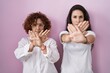 © Krakenimages.com - Hispanic mother and daughter wearing casual white t shirt over pink background rejection expression crossing arms and palms doing negative sign, angry face