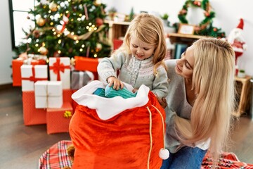 Wall Mural - Mother and daughter holding gifts on christmas bag sitting on the floor at home