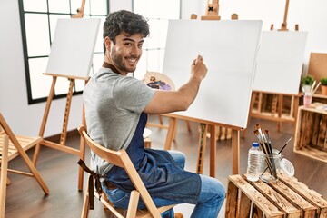 Wall Mural - Young hispanic artist man smiling happy painting at art studio.