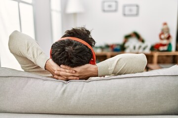 Canvas Print - Young hispanic man on back view using headphones sitting on the sofa with hands on head at home.