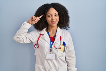 Poster - Young african american woman wearing doctor uniform and stethoscope smiling pointing to head with one finger, great idea or thought, good memory