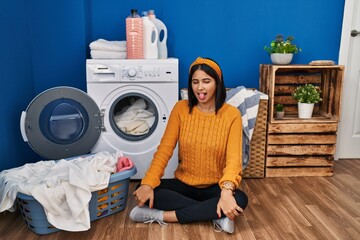 Poster - young hispanic woman doing laundry sticking tongue out happy with funny expression. emotion concept.