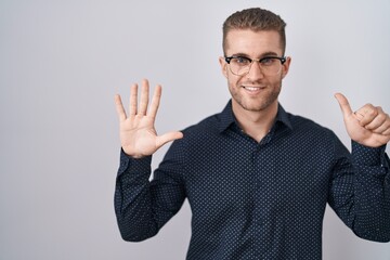 Sticker - Young caucasian man standing over isolated background showing and pointing up with fingers number six while smiling confident and happy.