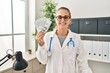 Young doctor woman holding dollars banknotes looking positive and happy standing and smiling with a confident smile showing teeth