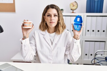 Sticker - Young hispanic woman working at dentist clinic holding brackets and aligner relaxed with serious expression on face. simple and natural looking at the camera.