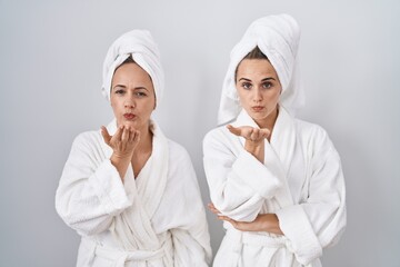 Wall Mural - Middle age woman and daughter wearing white bathrobe and towel looking at the camera blowing a kiss with hand on air being lovely and sexy. love expression.