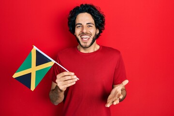 Wall Mural - Handsome hispanic man holding jamaica flag celebrating achievement with happy smile and winner expression with raised hand